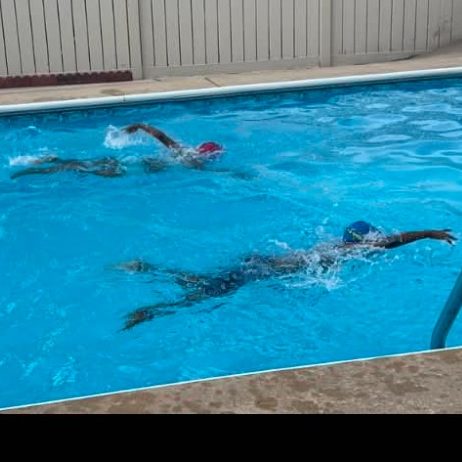 Two children in the pool on opposite sides, both swimming freestyle with their faces in the water.