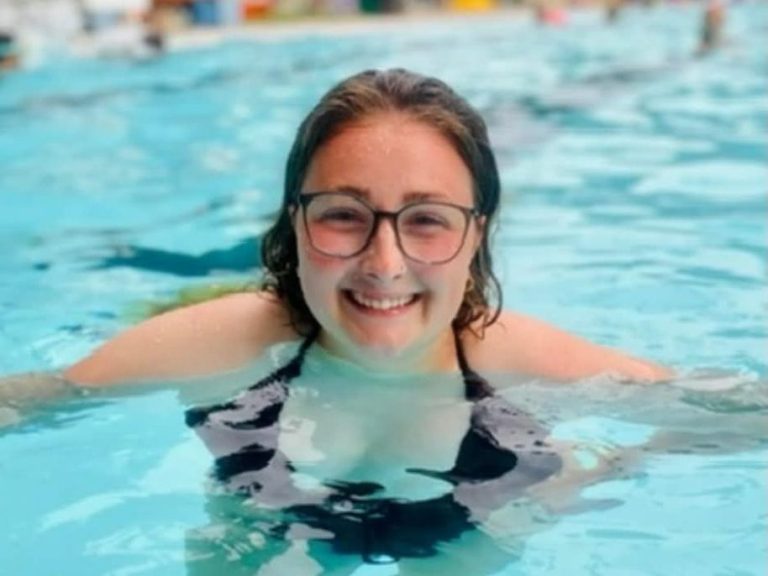 Image of swim instructor Keara smiling in the pool, wearing dark blue glasses and a black swimsuit.