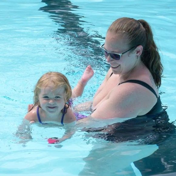 Mother and 1 year old daughter smiling and swimming in the pool together.