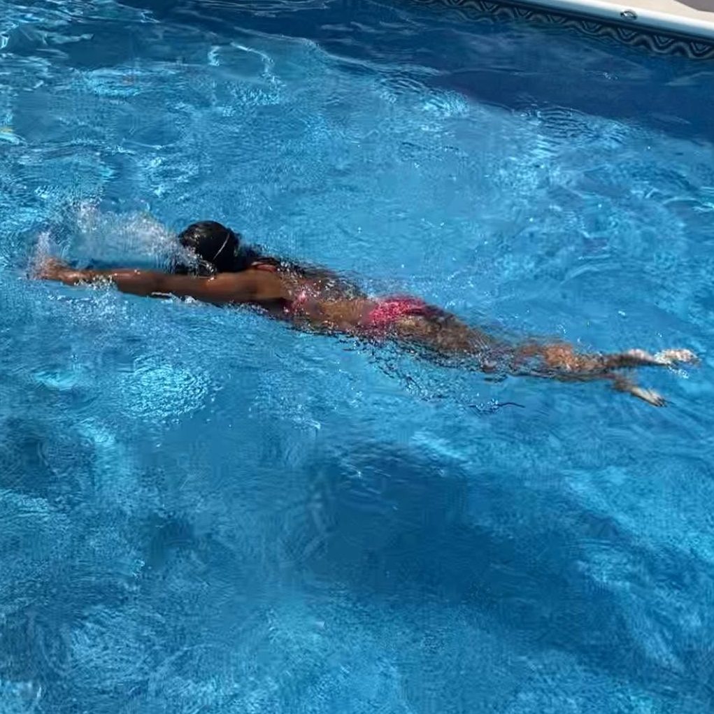 A child in the pool independently swimming freestyle with her face in the water.